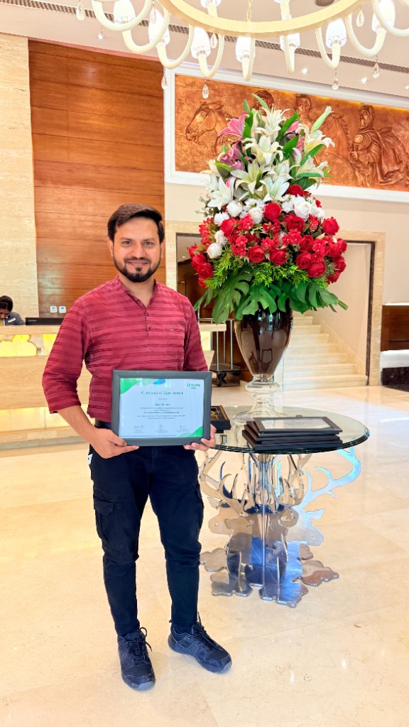 Ajaz Ahmad holding a certificate in a hotel lobby