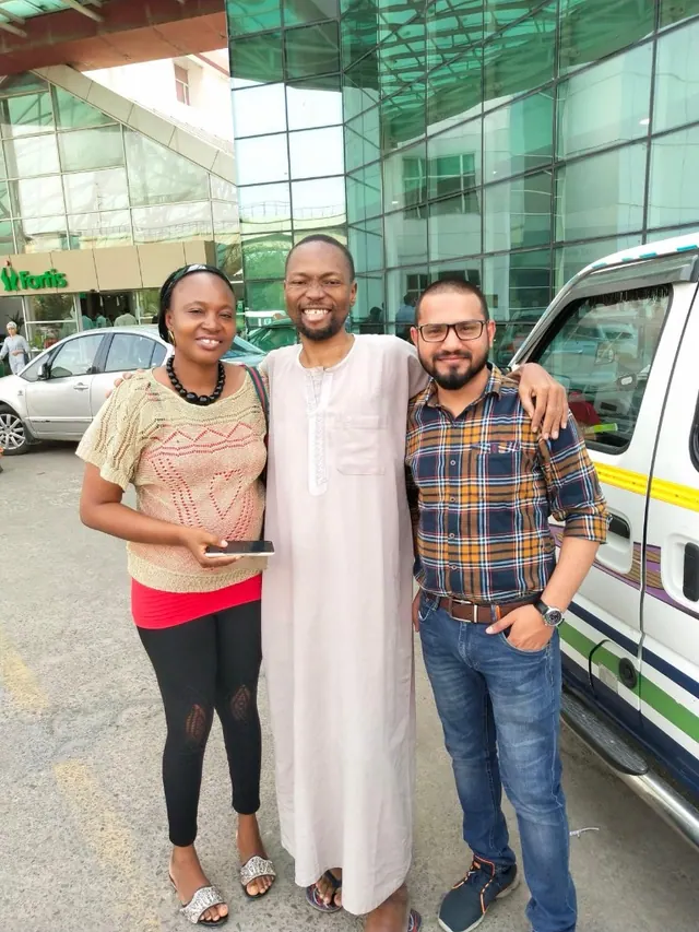 A patient and two men standing beside a car